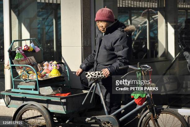 An elderly woman waits for customers to buy her dolls on the last day of the Chinese New Year holiday in Beijing on February 12, 2008. Millions of...