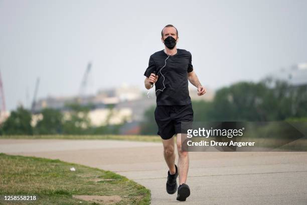 Jogger wears a face mask due to a code orange air quality alert because of smoke from Canadian wildfires on June 9, 2023 in Washington, DC. Compared...