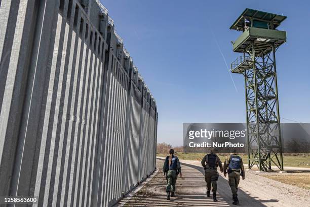 Border police walking alongside the fortification fence with a watch tower post in the background for police and the military equipped with camera...