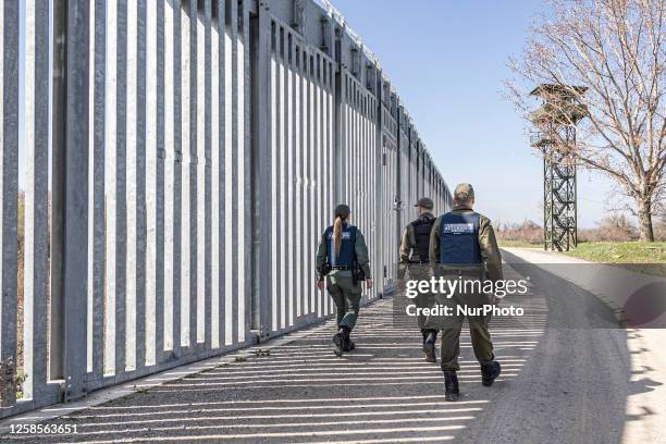 Border police walking alongside the fortification fence with a watch tower post in the background for police and the military equipped with camera...