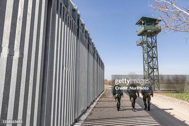 Border police walking alongside the fortification fence with a watch tower post in the background for police and the military equipped with camera...