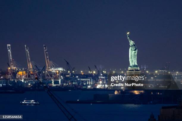 Statue of Liberty as seen from Brooklyn Bridge during the night with the lights from New Jersey visible and the ferry, the Liberty Island next to...