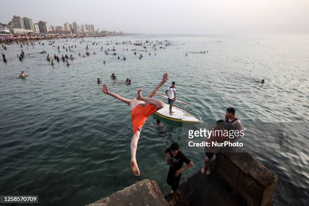 Palestinian youth is jumping into the sea as hundreds of Palestinians gather on Gaza Beach to cool off on a hot day during the sunset on Friday, June...