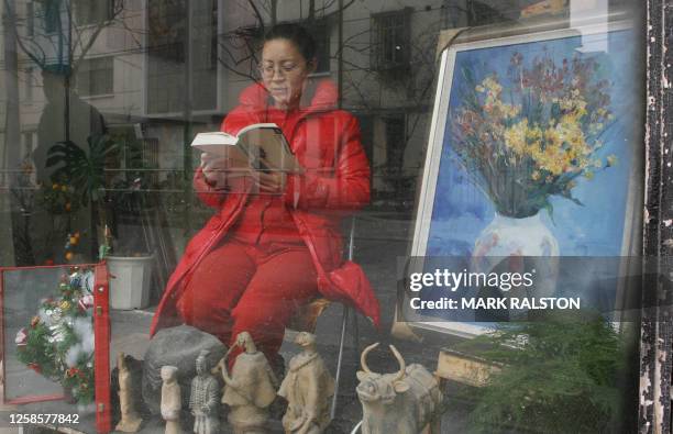 An art dealer sits in the window of her small gallery to catch some sun after light snow fell in Shanghai 17 February 2006. Snow is rare in the city...