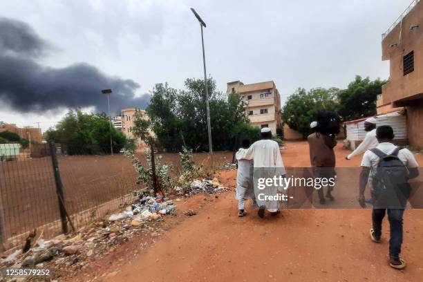 Smoke rises above buildings as people flee with some belongings, in Khartoum on June 10, 2023. A 24-hour ceasefire took effect on June 10 between...