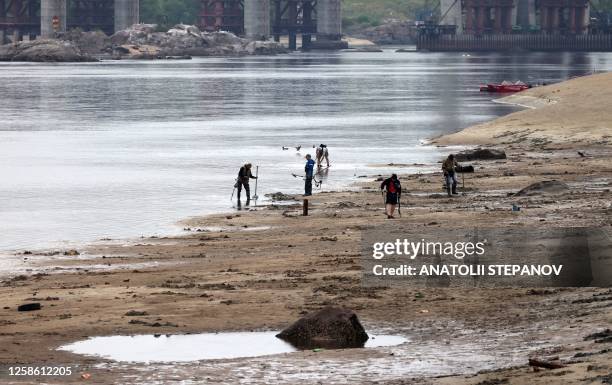 Residents use metal detectors to search the muddy banks exposed by the receding waters of the Dnipro river on the central beach of Zaporizhzhia on...