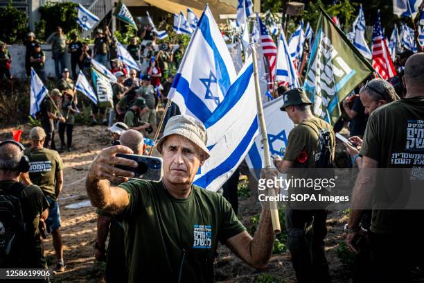 Protester takes a selfie while standing among Israeli active and veteran reserve soldiers from the Brother's in Arms activist group holding Israeli...