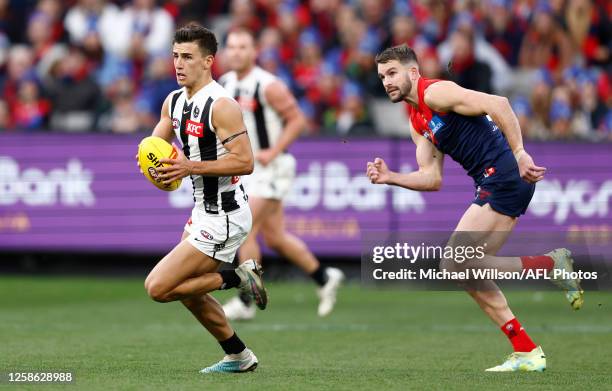 Nick Daicos of the Magpies is chased by Joel Smith of the Demons during the 2023 AFL Round 13 match between the Melbourne Demons and the Collingwood...