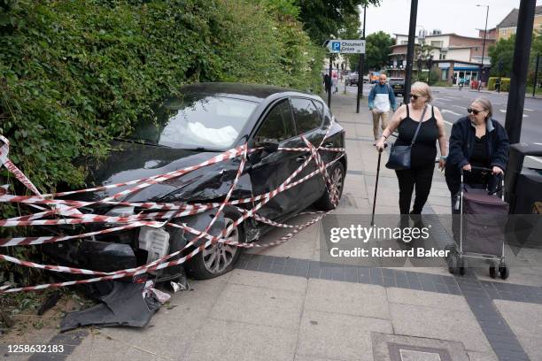 Pedestrians look at a wrecked hatchback car that mounted the pavement crushing bike barriers and which remains in an urban hedge outside Harris...