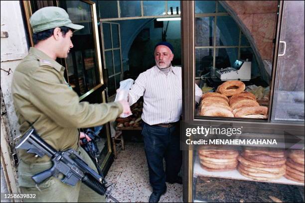 Palestinian baker Ahmad Mahfouz Abu Sneineh sells, 10 April 1987 in Jewish quarter of Jerusalem's Old City bread to a passing Israeli soldier during...