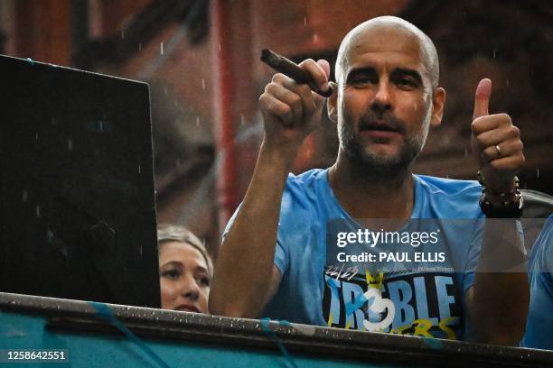 Manchester City's Spanish manager Pep Guardiola smokes a cigar as he celebrates with his players during an open-top bus victory parade in the streets...