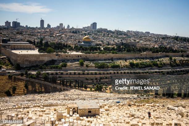 Jewish man works at a cemetery on the Mount of Olives overlooking the old city of Jerusalem on June 12, 2023.