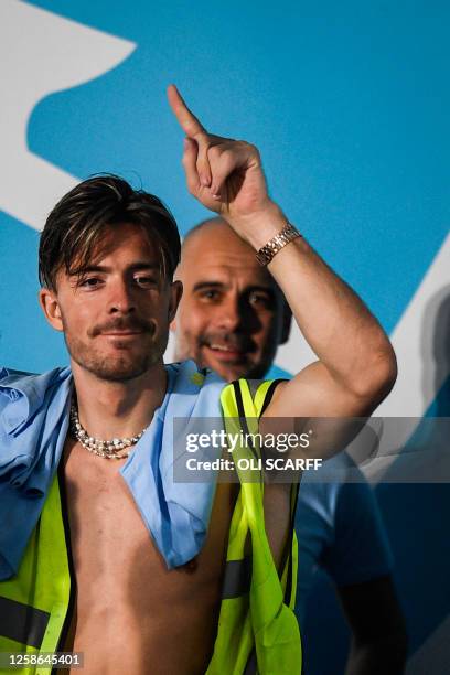 Manchester City's English midfielder Jack Grealish celebrates next to Manchester City's Spanish manager Pep Guardiola on stage following an open-top...