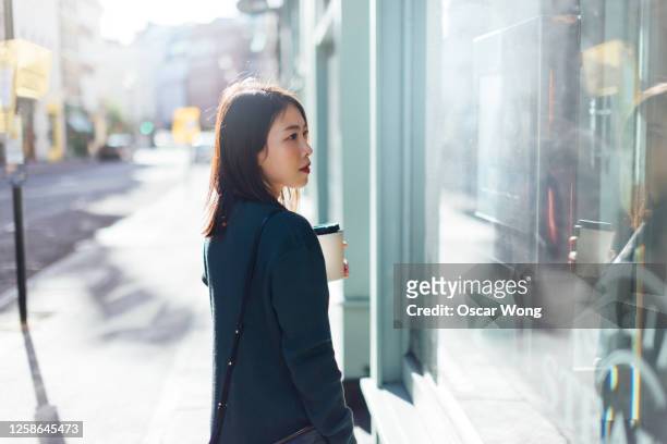 young woman holding take-away coffee while shopping on the high street - store window stock pictures, royalty-free photos & images