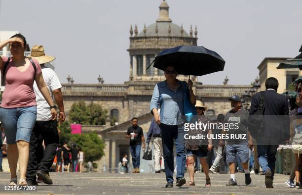 Group of people try to protect themselves from the intense sun during one of the hottest days of the third heat wave earlier this week that will see...