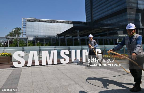 Workers water the flower garden next to the logo of Samsung Electronics at the company's headquarters in Suwon on June 13, 2023.