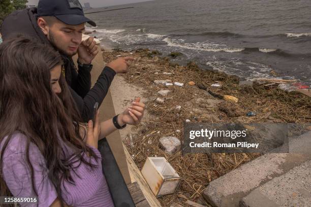 People look at a polluted beach with objects some of which presumably were washed down the Dnipro River as the result of the Kakhovka dam destruction...