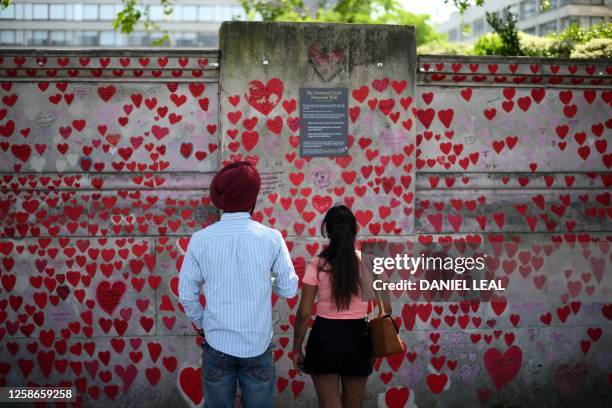 People look at messages and hearts on the National Covid Memorial Wall, dedicated to those who lost their lives to Covid-19, on the embankment on the...