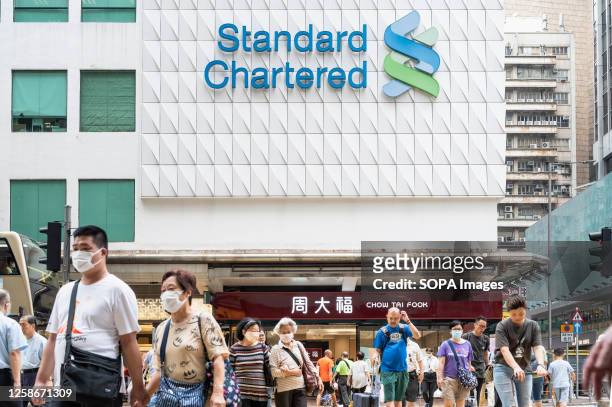 Pedestrians cross the street in front of the British multinational banking and financial services company Standard Chartered branch seen in Hong Kong.