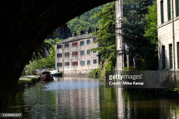 Scene of old industrial mill buildings along the Rochdale Canal seen through a towpath tunnel on 7th June 2023 in Hebden Bridge, United Kingdom. In...