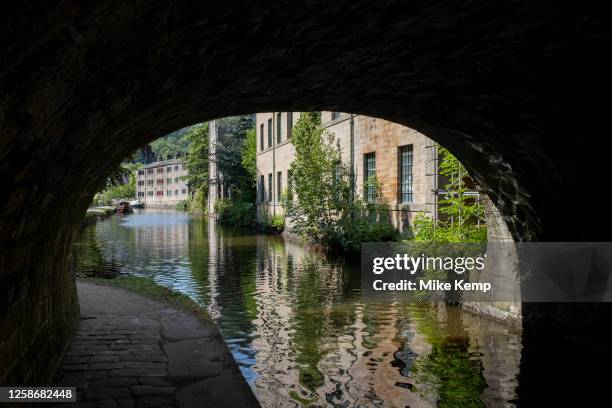 Scene of old industrial mill buildings along the Rochdale Canal seen through a towpath tunnel on 7th June 2023 in Hebden Bridge, United Kingdom. In...