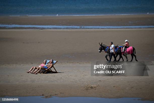 People sunbathe sit in deckchairs to sunbathe on the beach, as visitors take a donkey ride across the sand, in the sunshine in Blackpool, north west...