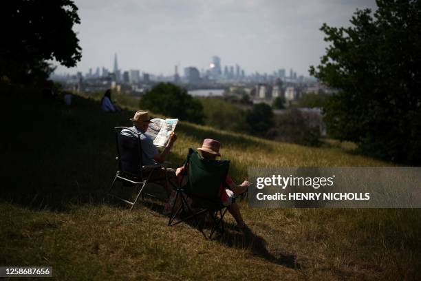 Couple sit on camping chairs and read the newspaper while enjoying the sun at Greenwich Park, in south east London on June 14, 2023. A high air...