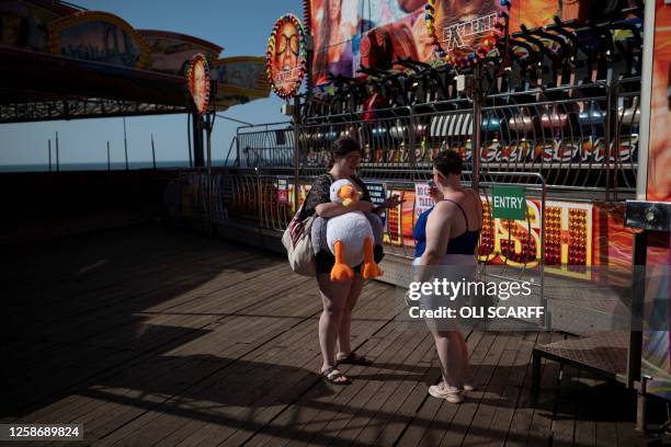 Two women speak next to the attractions at Blackpool Central Pier, in Blackpool, north west England, on a sunny day, on June 14, 2023.