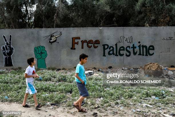 Two boys walk along a wall bearing graffiti in Deir al-Balah in the central Gaza Strip on June 14, 2023.