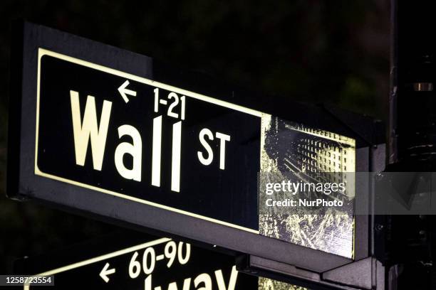 Wall Street sign inscription as seen illuminated with light during the night on the road and buildings at Wall St address, downtown in lower...