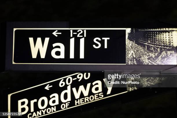 Wall Street and Broadway sign inscription as seen illuminated with light during the night on the road and buildings at Wall St address, downtown in...