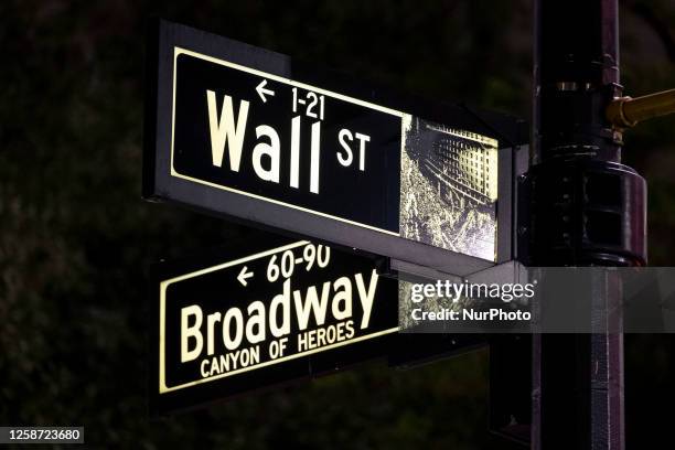 Wall Street and Broadway sign inscription as seen illuminated with light during the night on the road and buildings at Wall St address, downtown in...