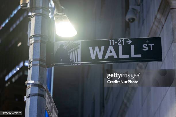 Wall Street sign inscription as seen illuminated with light during the night on the road and buildings at Wall St address, downtown in lower...