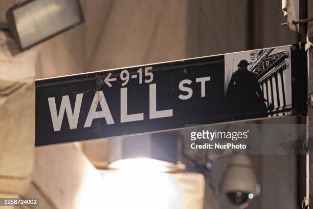 Wall Street sign inscription as seen illuminated with light during the night on the road and buildings at Wall St address, downtown in lower...