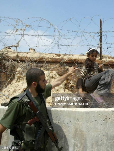 Hamas security guard helps a Palestinian girl negotiate the barbed wire fence that separates Rafah in the southern Gaza Strip from Egypt on July 23...