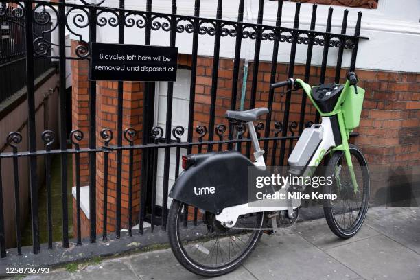 Lime bike in Knightsbridge next to a sign on a fence which reads 'Bicycles left here will be removed and disposed of' on 23rd May 2023 in London,...