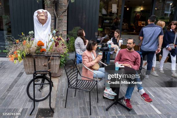 Two people enjoy a foccee beside a model of ET in a bicycle basket as people gather to hang out outside restaurants, bars and cafes on Pavillion Road...