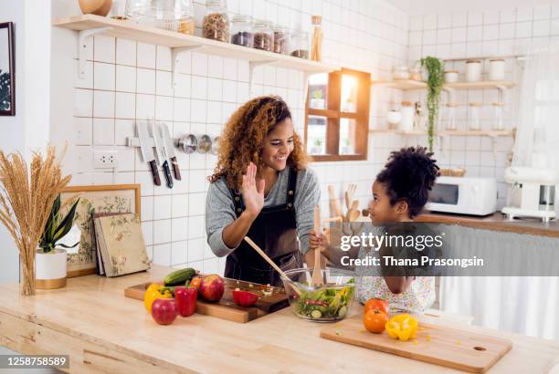 mother and daughter having fun with the vegetables - black mother and child cooking stock-fotos und bilder
