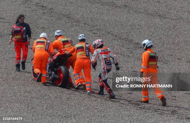 Repsol Honda Team's Spanish rider Marc Marquez is assisted by staff members after crashing a second time during the qualifying session for the MotoGP...