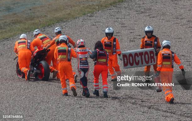 Repsol Honda Team's Spanish rider Marc Marquez is assisted by staff members after crashing a second time during the qualifying session for the MotoGP...