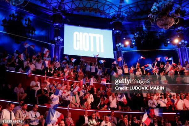 Supporters wave French flags below a giant screen displaying President of the French right-wing party Les Republicains and MP Eric Ciotti's name...