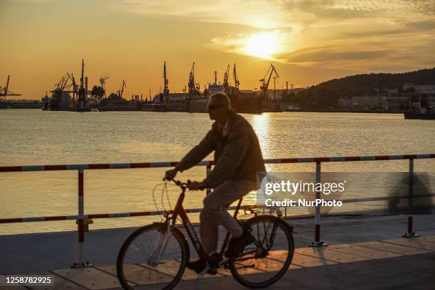 Man on the bike passing the port canal with a view of the Naval Shipyard and Gdynia Port during the sunset is seen in port of Gdynia, Poland on 17...