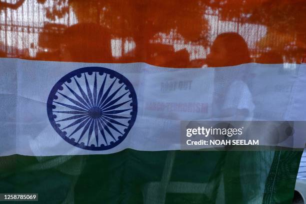 Members of the Hyderabad Manipur Society , seen through an Indian flag, hold placards during a protest amid ongoing ethnic violence in India's...