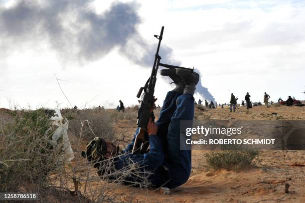 Libyan rebel fighter uses his legs to steady his machin-gun as he fires at a fighter jet flying overhead during clashes with forces loyal to leader...