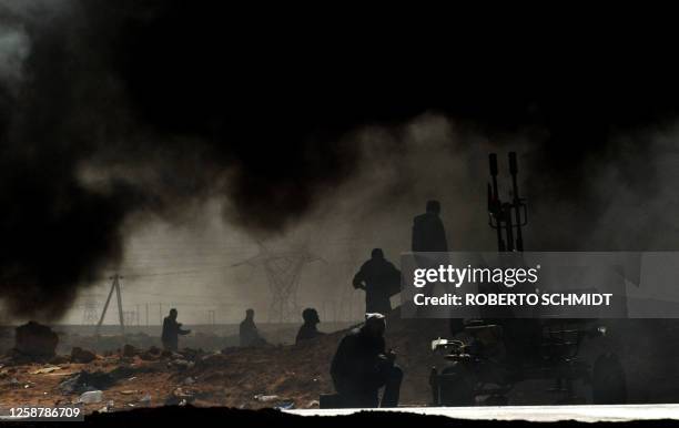 Libyan rebel fighters are surrounded by smoke as they sit near the front line on March 11, 2011 as rebels battled troops loyal to Moamer Kadhafi...