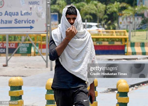 Commuters seen with their heads covered to protect them from the hot summer day at sector 52, on June 18, 2023 in Noida, India.