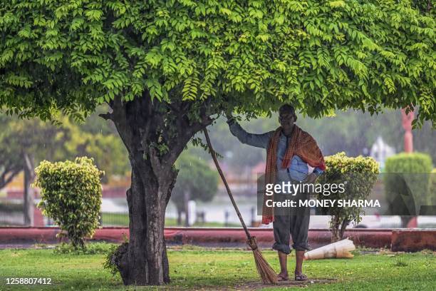 Civic worker takes cover under a tree as it rains in New Delhi, on June 19, 2023.
