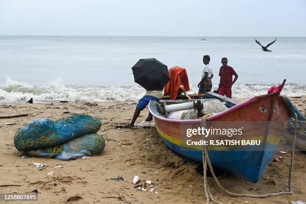 Fishermen wait along the Marina beach, as it rains in Chennai on June 19, 2023.