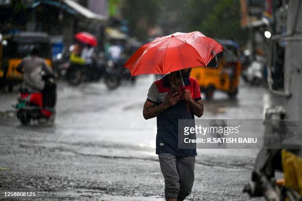 Man holds an umbrella while he walks along a street, as it rains in Chennai on June 19, 2023.