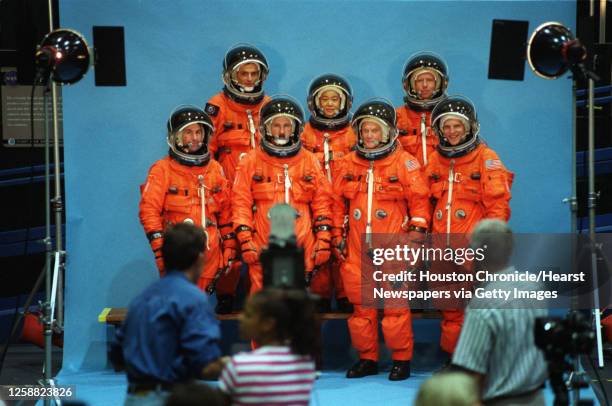 Worker adjusts an astronauts helmet as Discovery crew members pose for a new official photo at Johnson Space Center. Glenn, again, is bottom row,...